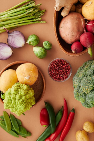 Assorted fresh vegetables, including bell peppers, carrots, and leafy greens, arranged on a wooden surface, ready for kitchen prep