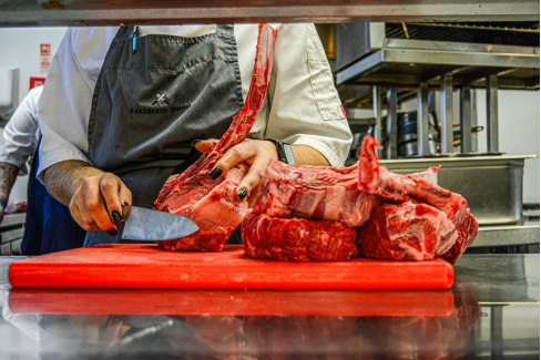 Chef preparing ribeye steaks in a professional kitchen, arranging cuts for cooking and plating.