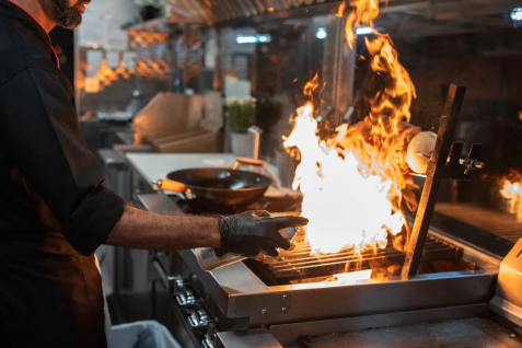 Chef cooking kebabs on a grill in a professional kitchen, preparing skewers for service.