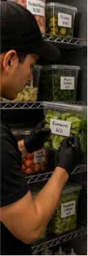 Kitchen worker labeling and dating food storage containers on refrigerator shelves for proper FIFO rotation